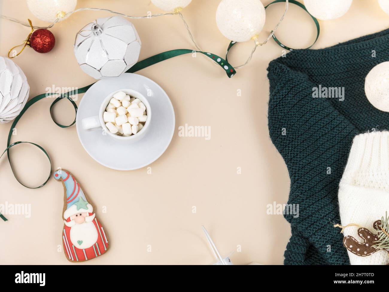 Cup of coffee, gift box and knitted sweater, led lights on beige background. Hygge style, winter concept. Cozy home desk. New year and Christmas Stock Photo