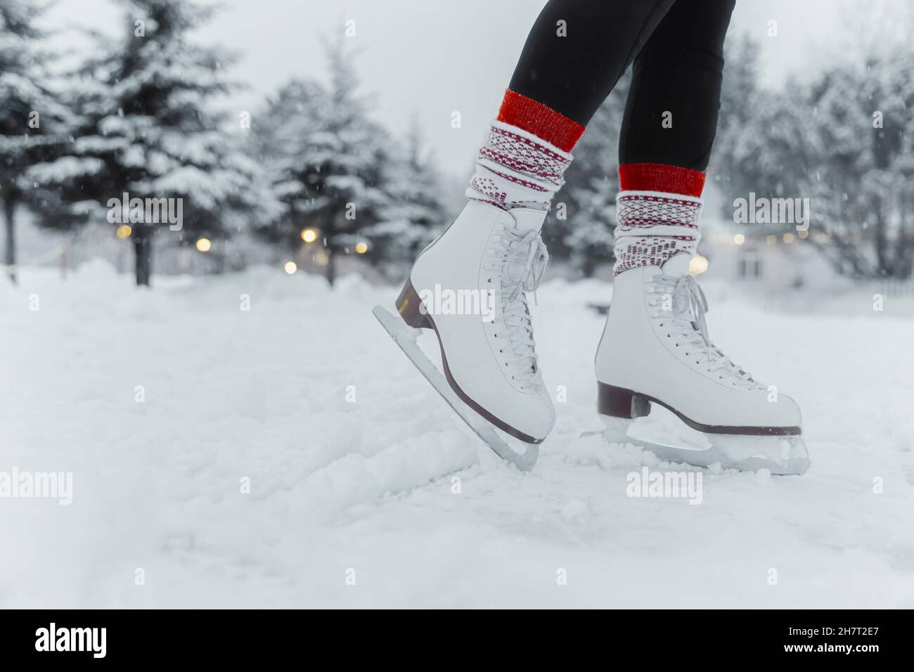 Figure skating woman skating on ice at outside rink during snowfall wearing female white leather boots. Family outdoor activity winter sport Stock Photo