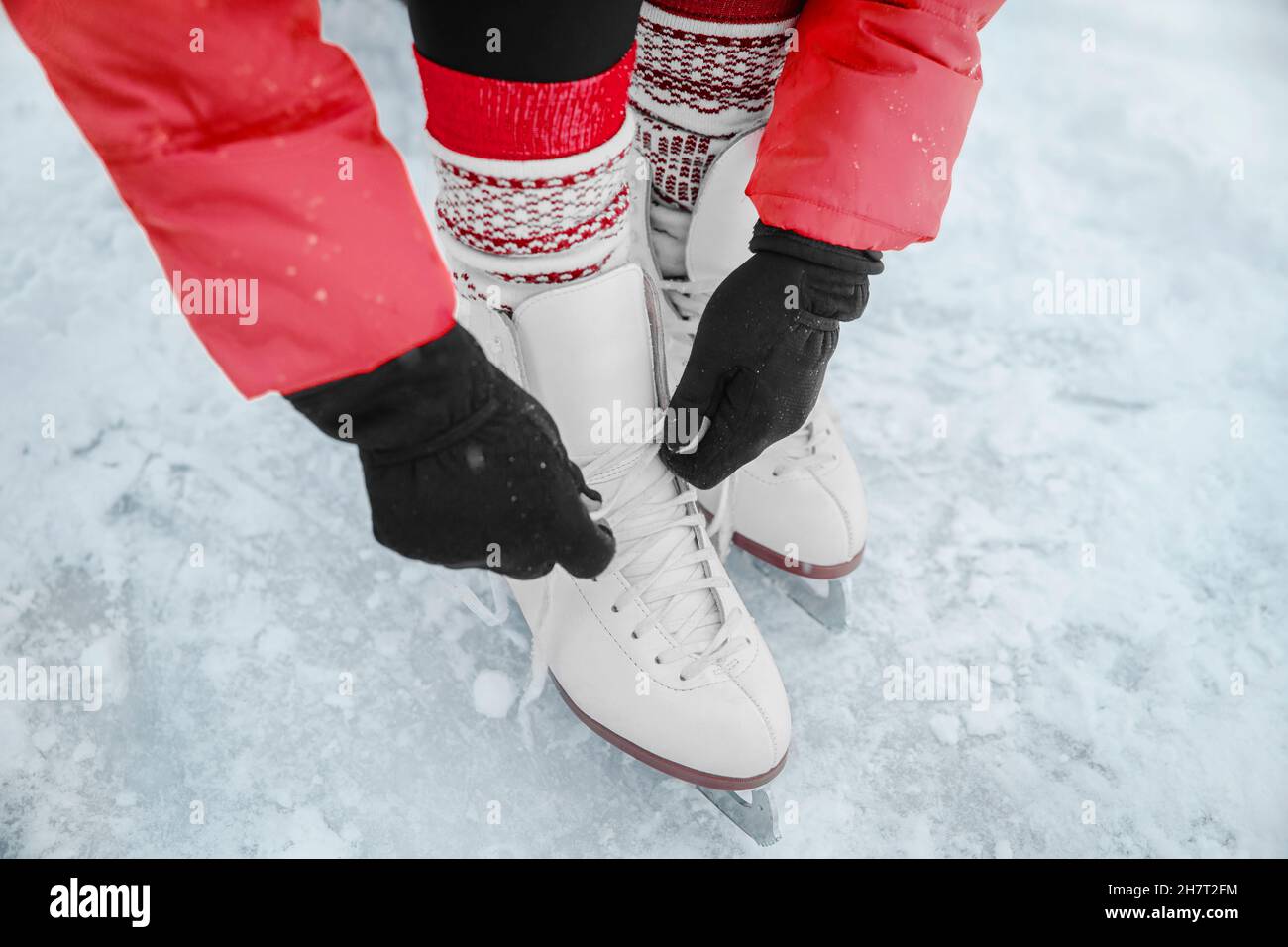 Ice skating woman tying laces of figure skates shoes to go skate at rink. Winter sport people. Closeup of hands and feet. Stock Photo