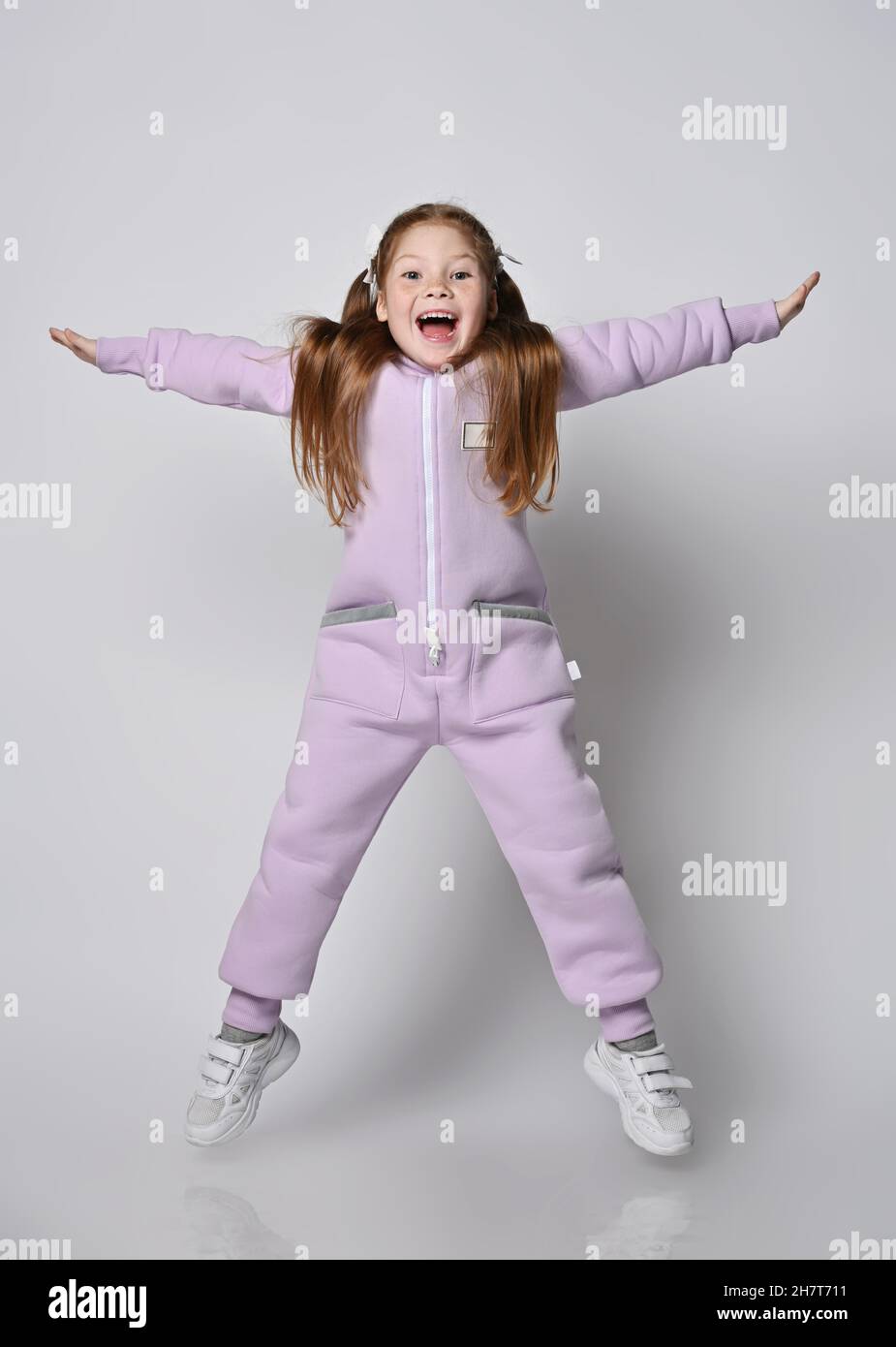 Active, frolic kid girl in pink jumpsuit with zipper jumps with legs and arms wide apart, happy screaming Stock Photo