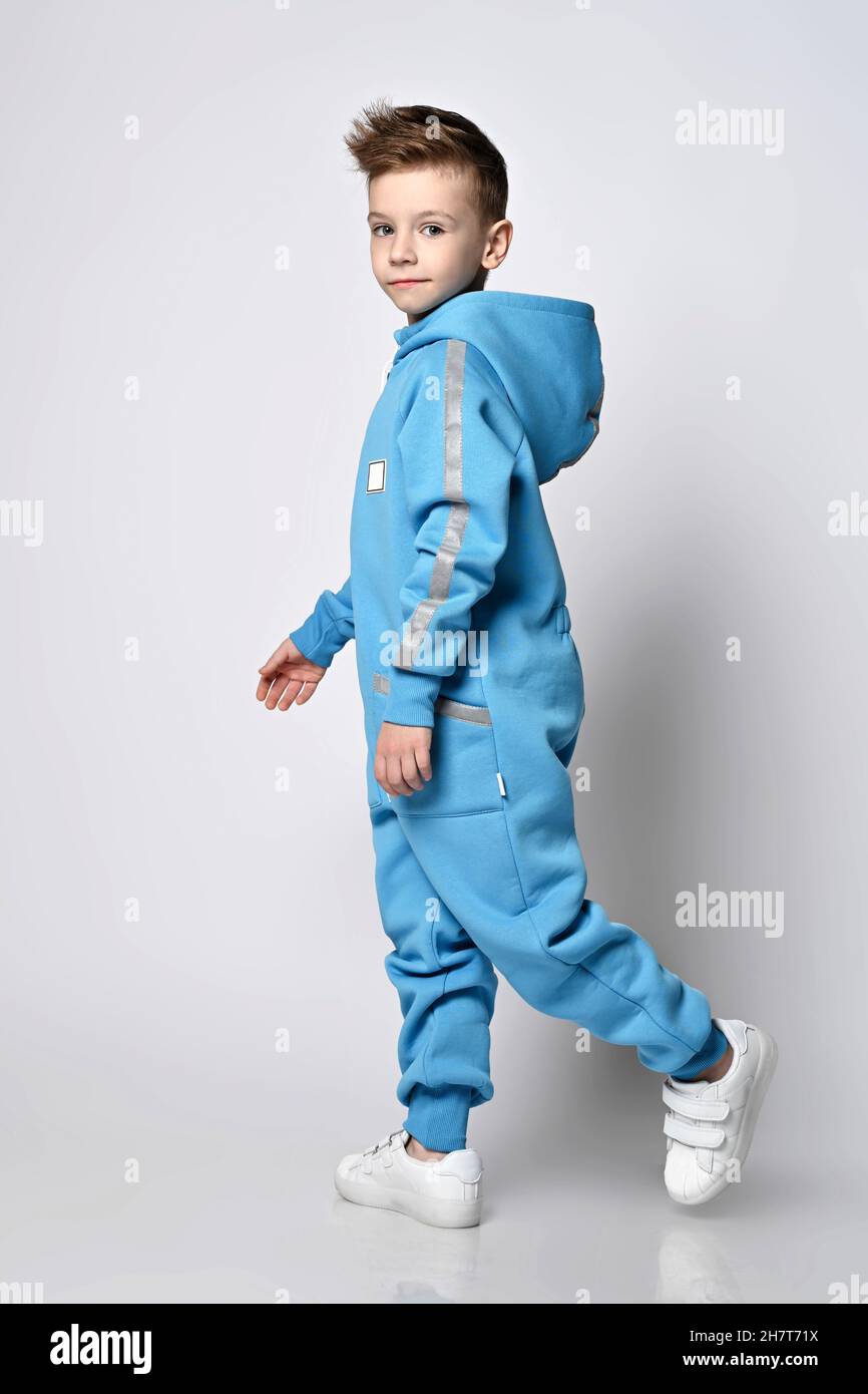 Frolic smiling kid boy in blue jumpsuit with hood and pockets with reflective stripes walks. Side view Stock Photo