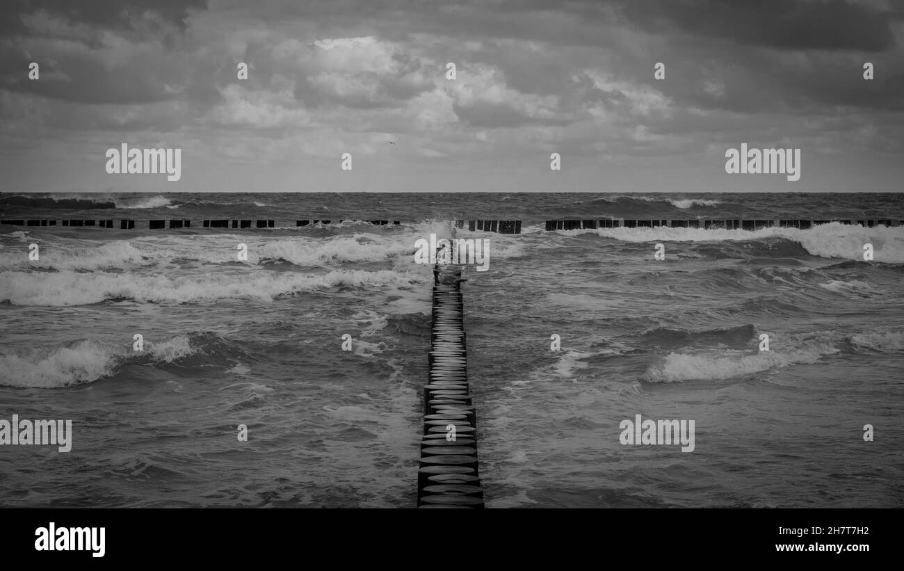 Grayscale shot of a long wooden trail over the stormy Baltic sea Stock Photo