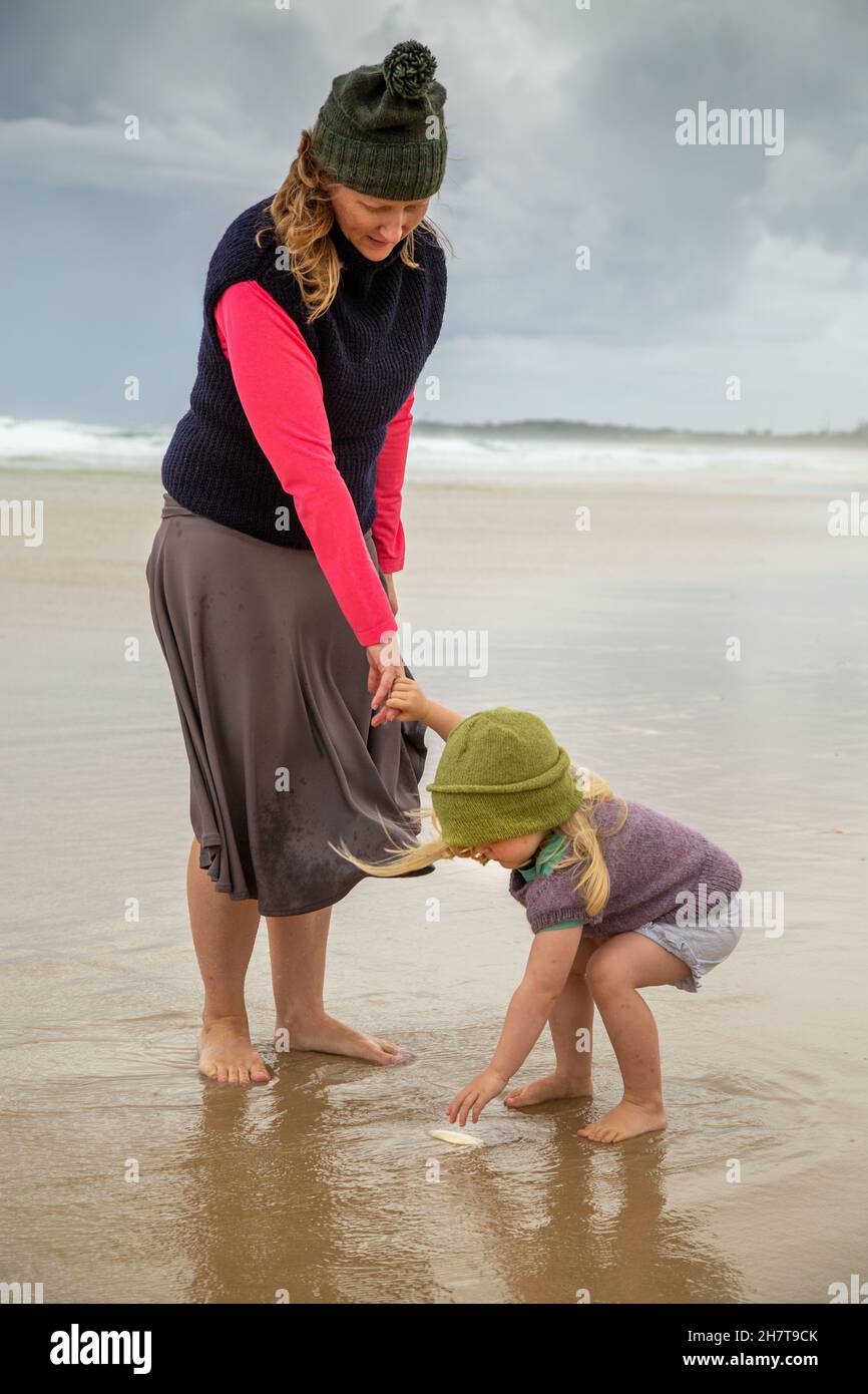 Blond mother and toddler daughter exploring at the beach on a stormy day. Stock Photo