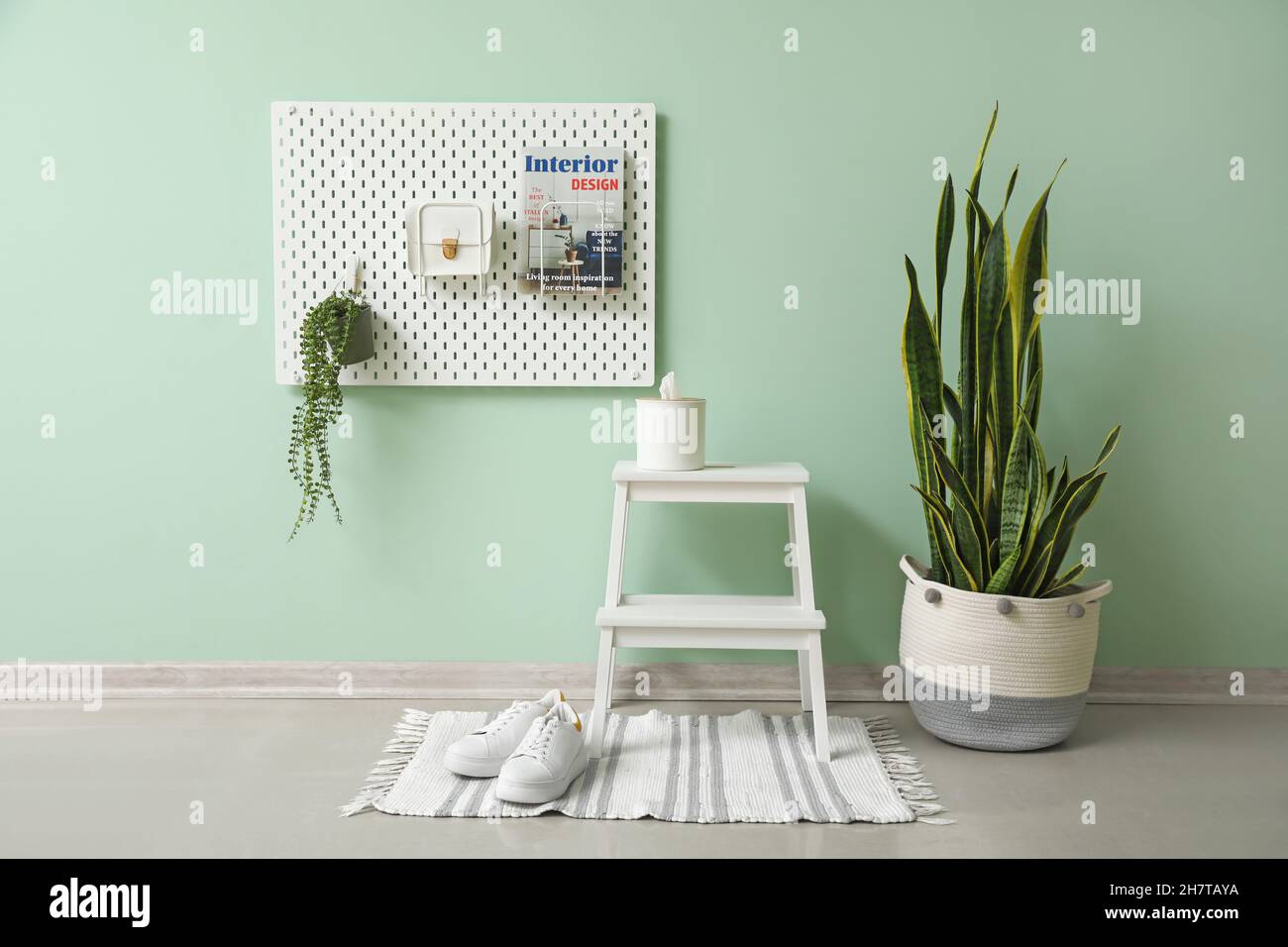 White step stool with tissue box and peg board hanging on green wall