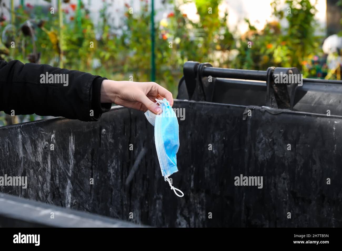 Woman throwing used medical mask into plastic container outdoors Stock ...