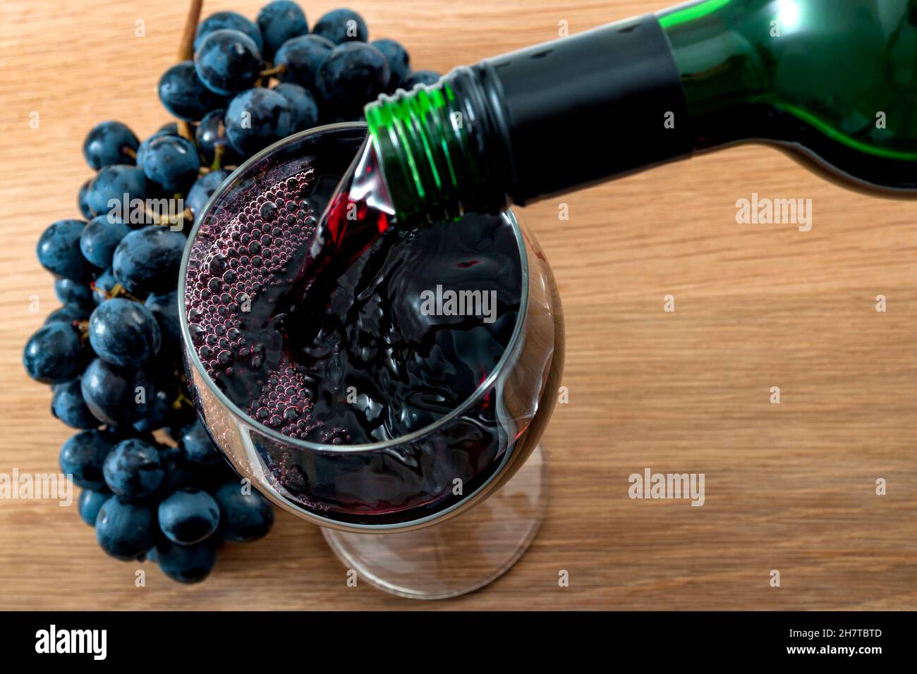 Alcoholic drink, wine making and alcohol industry concept with red wine pouring from a bottle into a glass on a wooden table in the rustic setting of Stock Photo