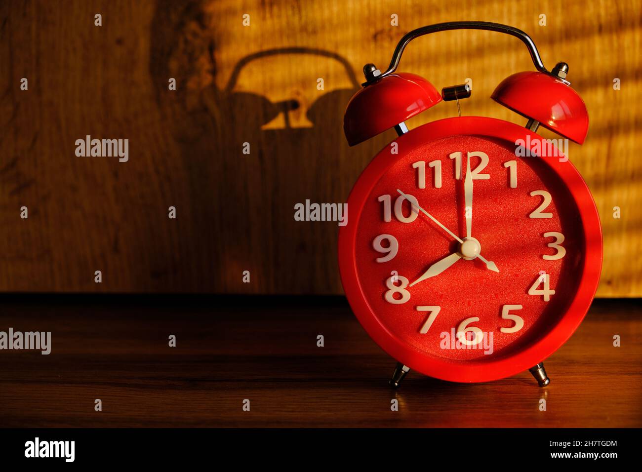 Red alarm clock early morning on table, shadows from blinds background