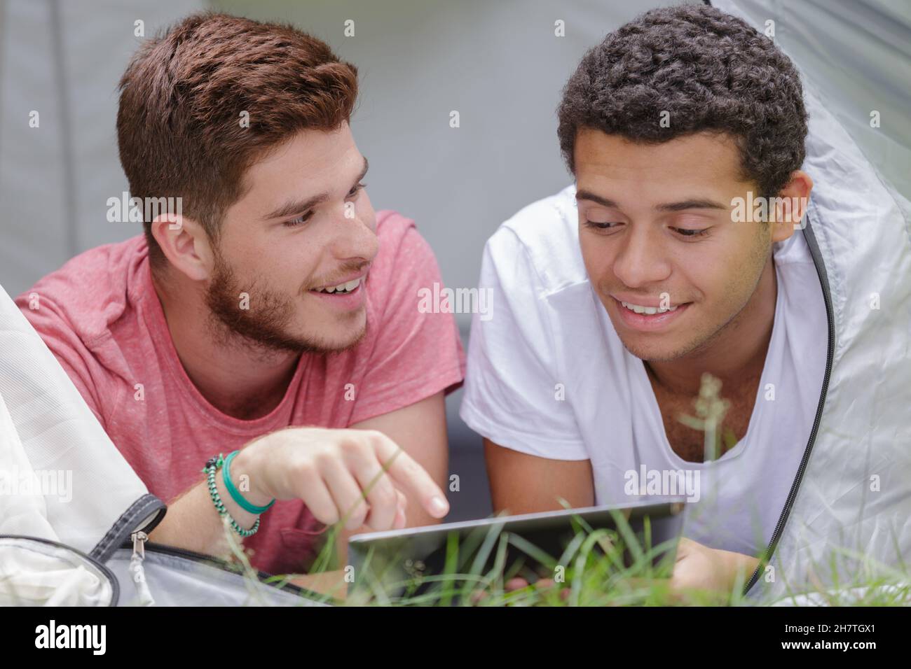 two young men layed in tent looking at tablet Stock Photo