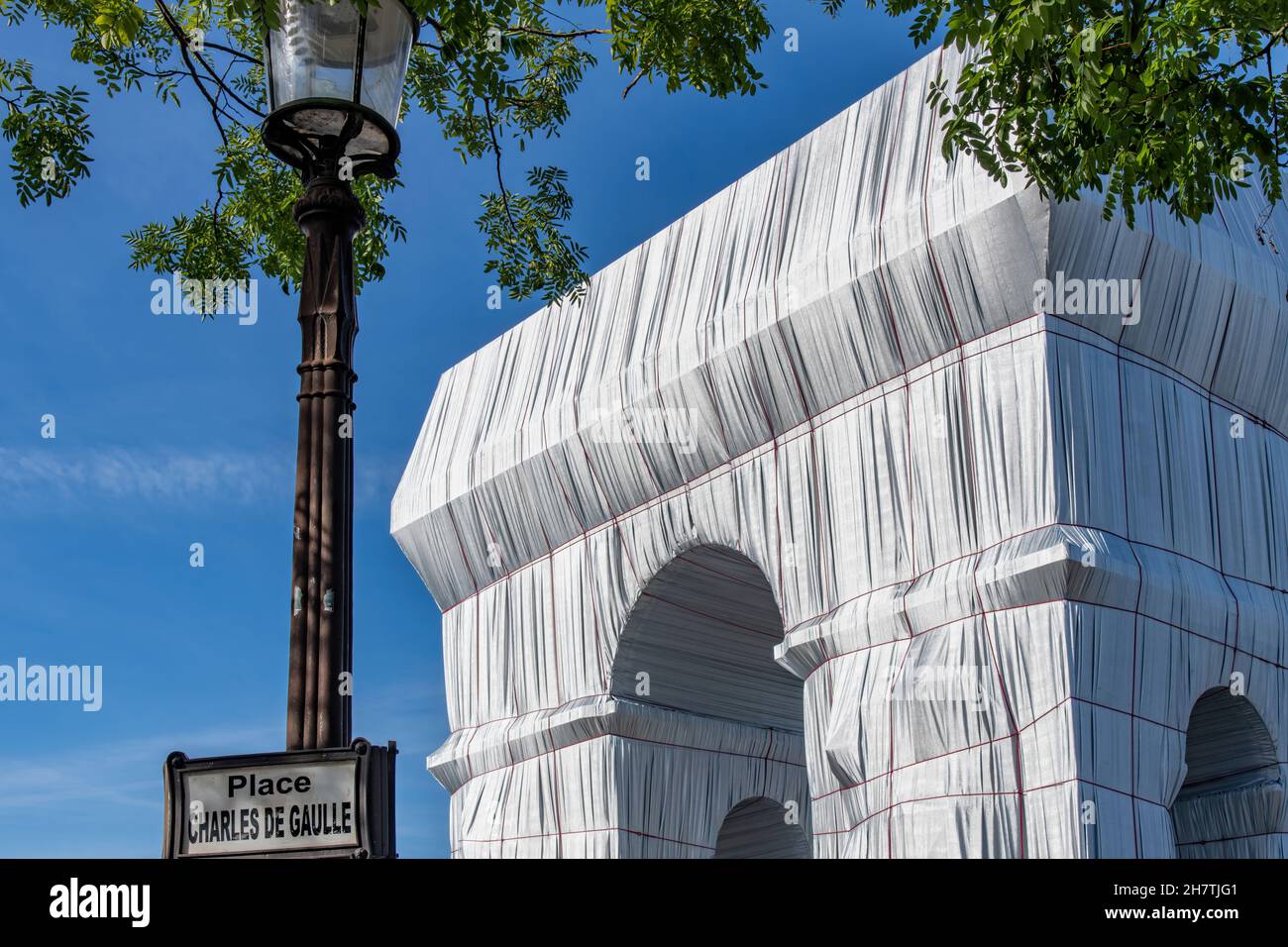 Paris, France-September 2021; Low angle partial view of wrapped Arc de Triomphe art installation by Christo with street lantern with street sign (Plac Stock Photo