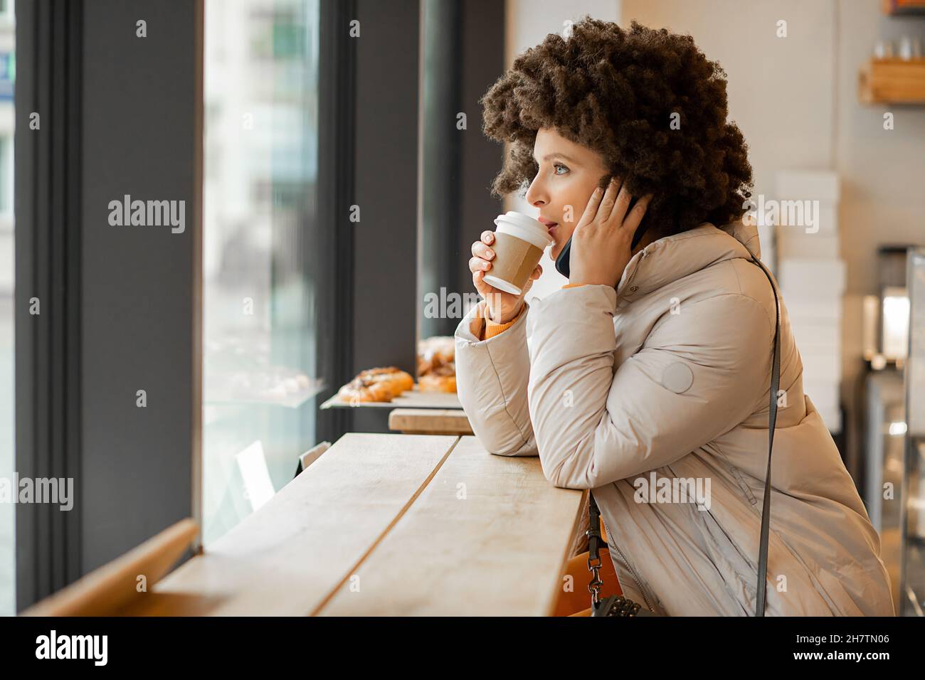 Woman with smart phone in cafe, Afro Hairstyle, drinking caffee or tea, looking through window, enjoying moment, happy hours Stock Photo