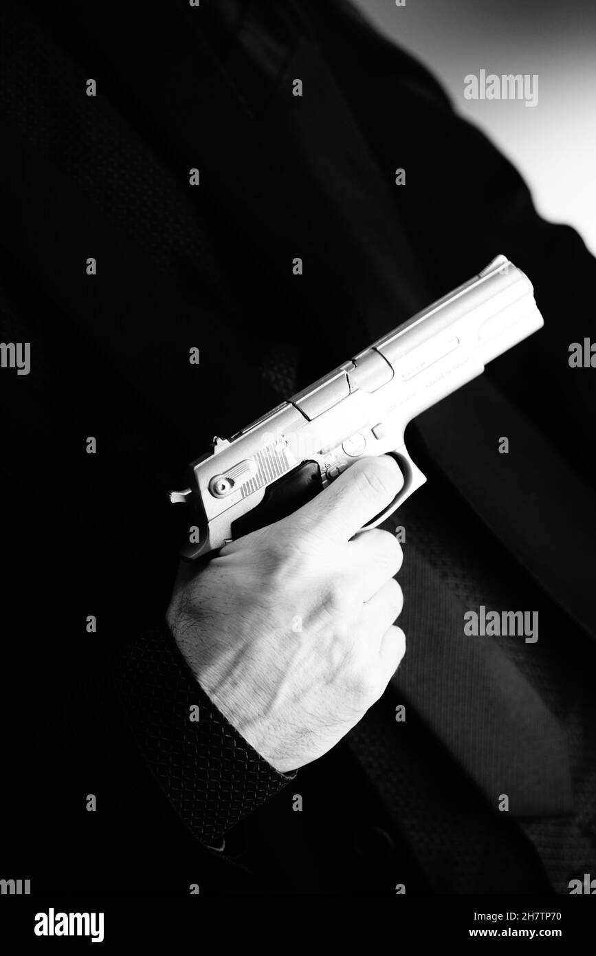 Well dressed male secret agent detective spy wearing suit and tie holding automatic pistol. Stock Photo