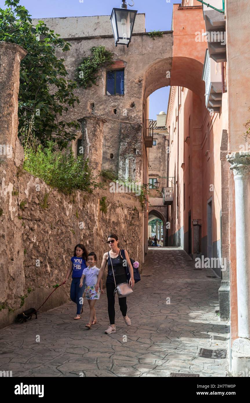 A woman with two girls and a small dog walking down a colorful street on a sunny day in Ravello, the Amalfi Coast, Italy. Vacation destination. Stock Photo