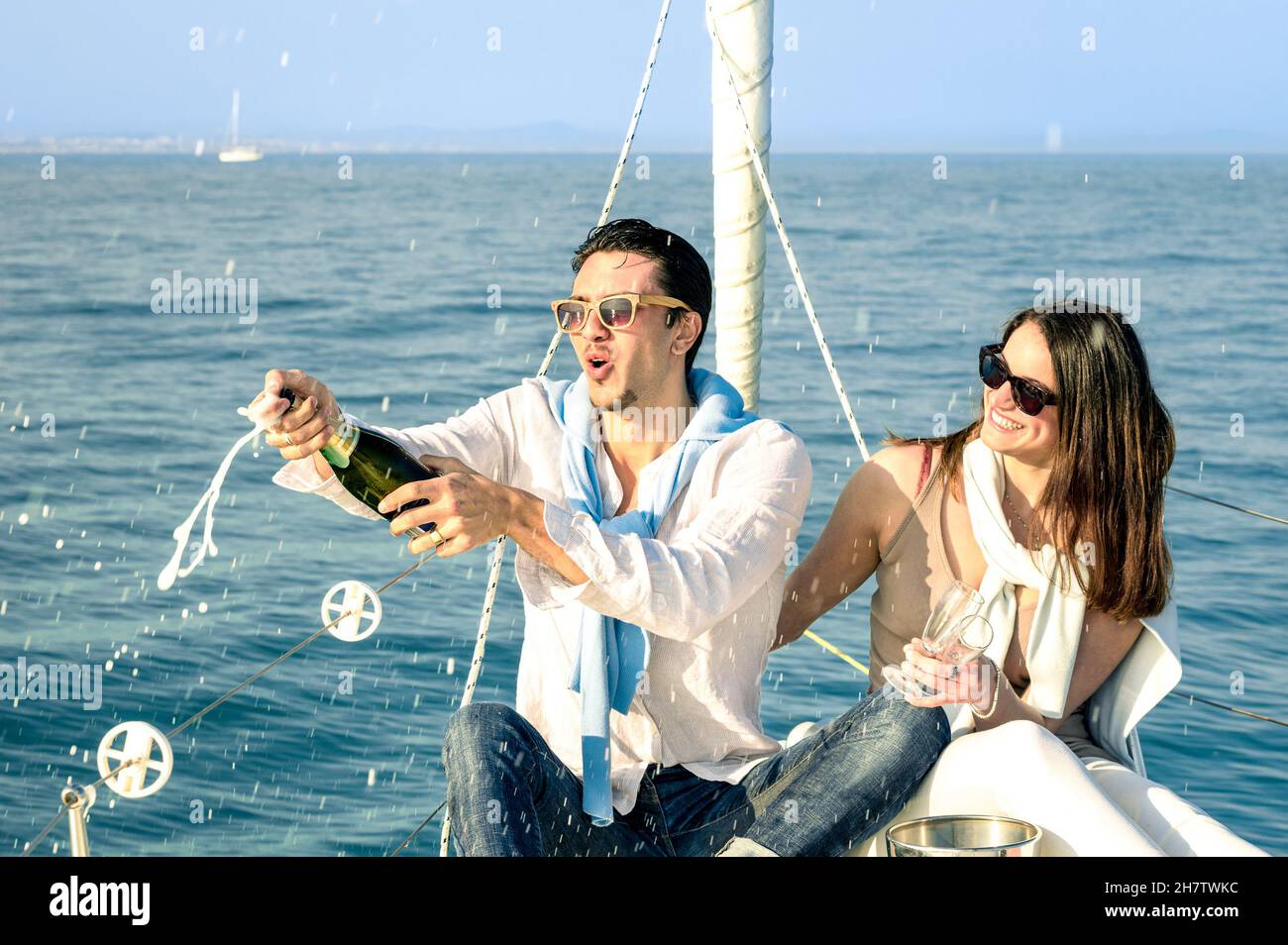 Young couple in love on sailing boat cheering with champagne wine bottle - Happy girlfriend birthday party cruise travel on luxury sailboat Stock Photo