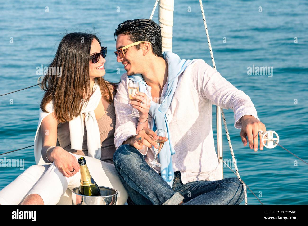 Young couple in love on sail boat with champagne flute glasses - Happy exclusive alternative lifestye concept - Boyfriend and girlfriend flirting Stock Photo
