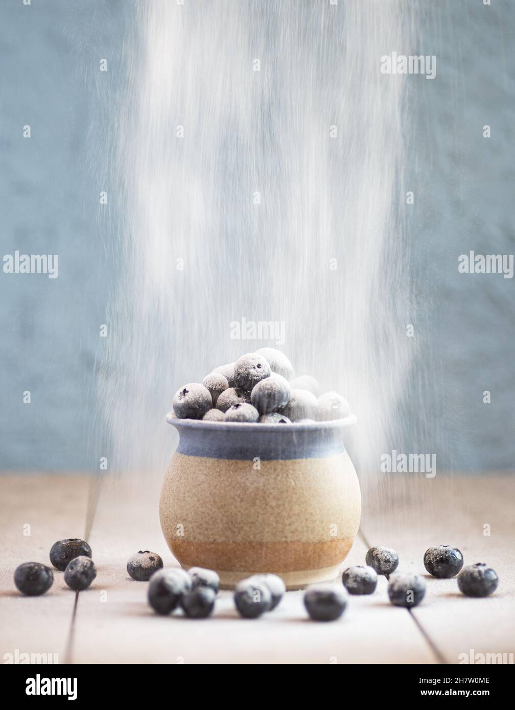 A stoneware cup filled with blueberries on a ceramic surface. Dusting powder sieved on to the berries Stock Photo