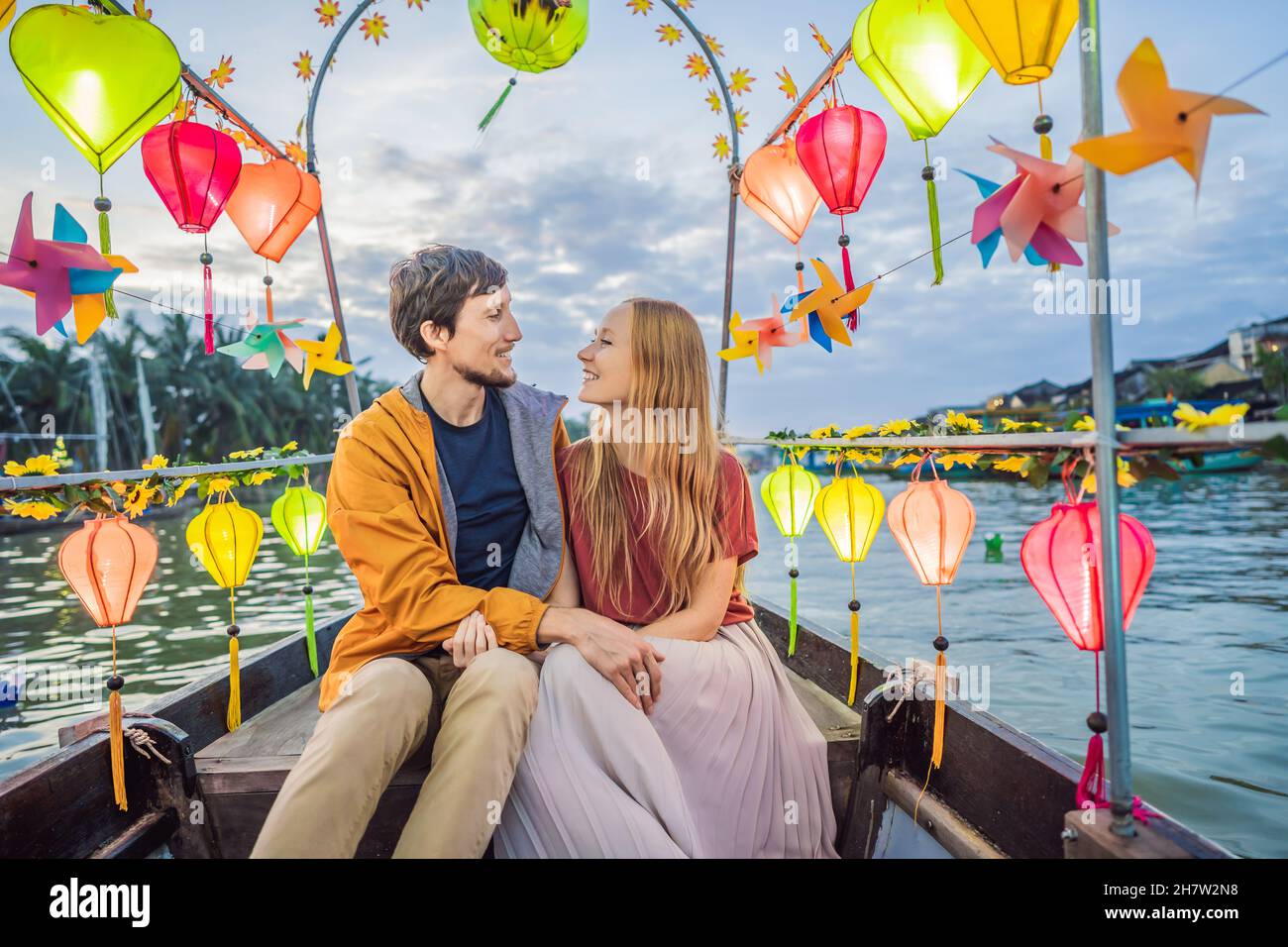 Happy couple of travelers ride a national boat on background of Hoi An ...