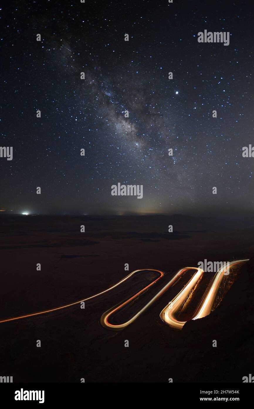 Car's light trails on a curvy road in the desert and the milky way in ...