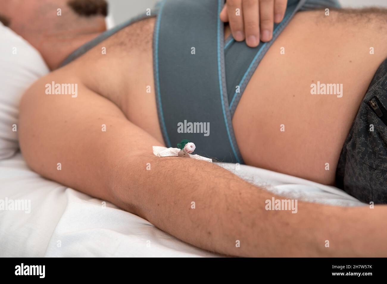 A patient young man with dropper catheter lying on bed in hospital ward. Traumatology Surgery medical procedure in the emergency. Elastic bandage shoulder fracture Stock Photo