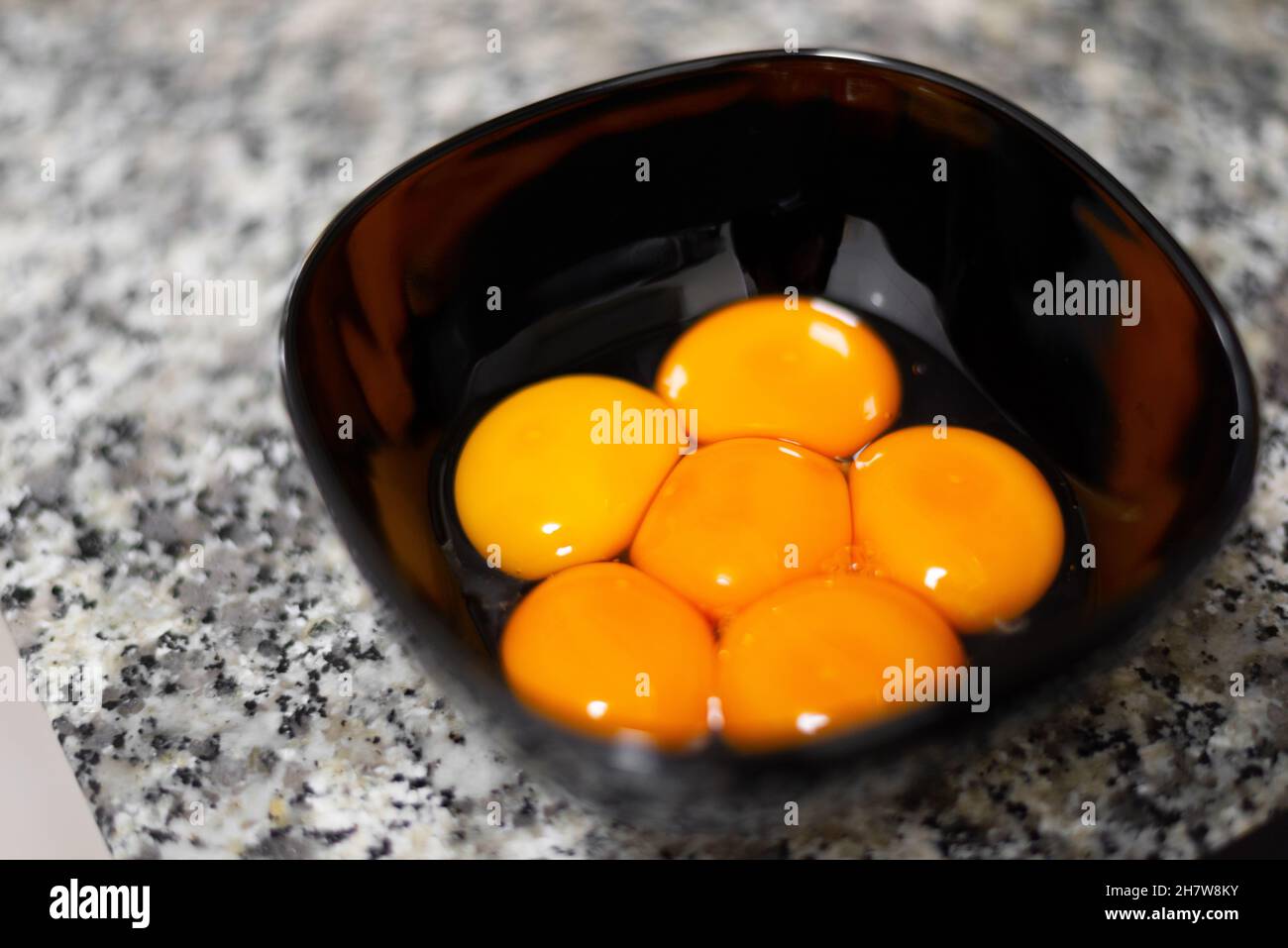 Egg yolks on a black bowl against a stone surface Stock Photo