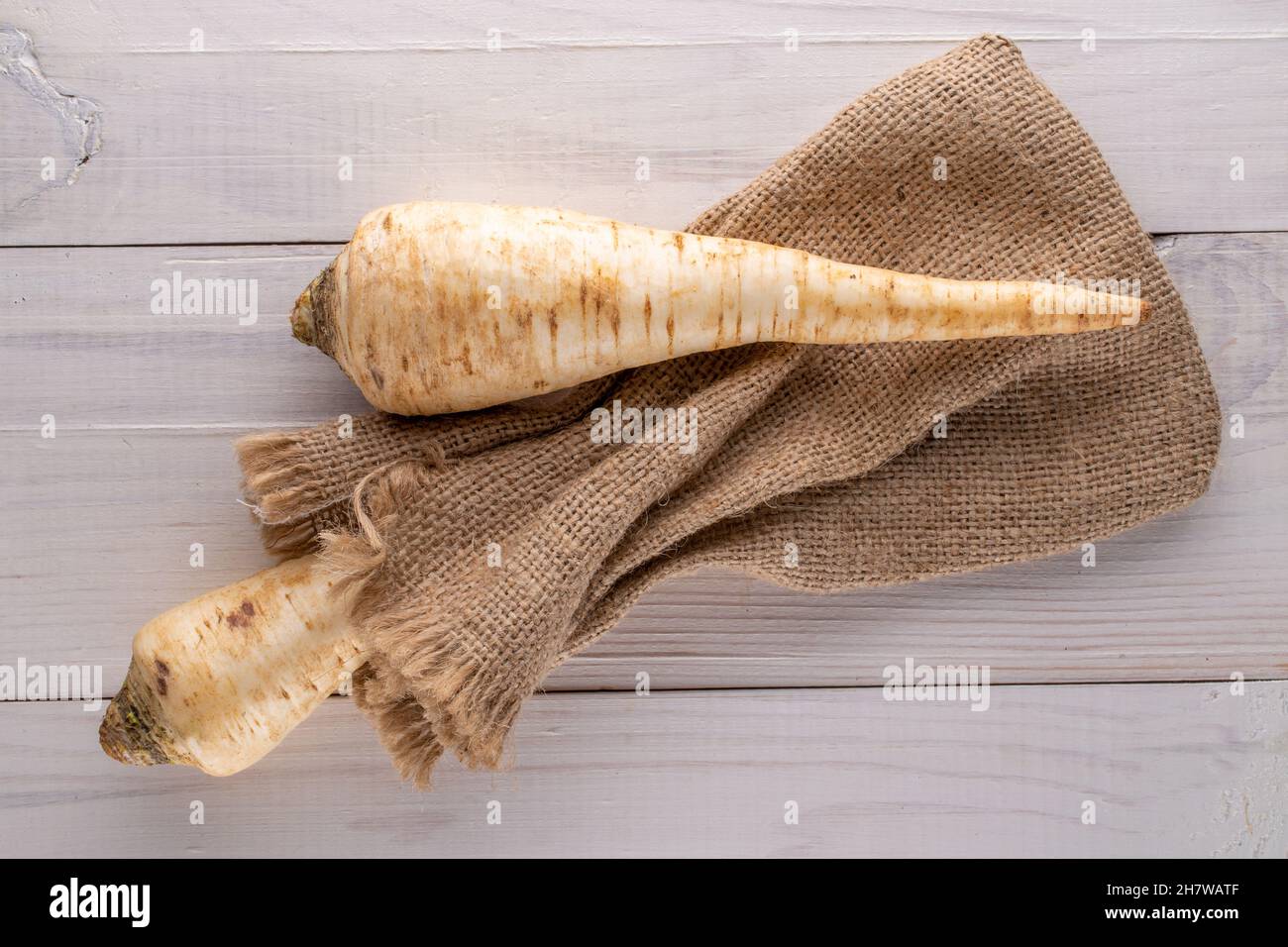 Two fragrant parsnip roots with a jute bag on a wooden table, close-up, top view. Stock Photo