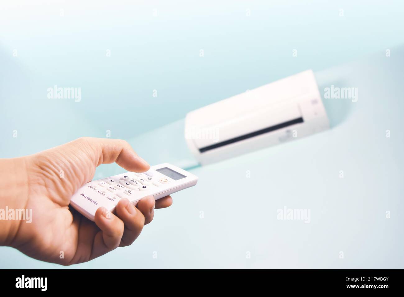 The air conditioner remote control is pressed by a human hand to