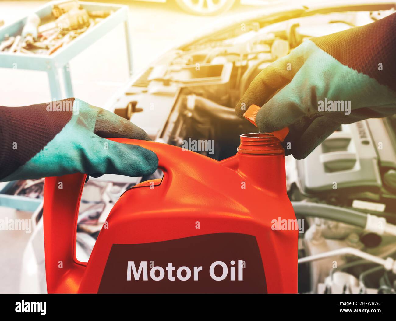 Mechanic opens the cap of a red colored gallon of motor oil to refill the car engine in the repair shop Stock Photo