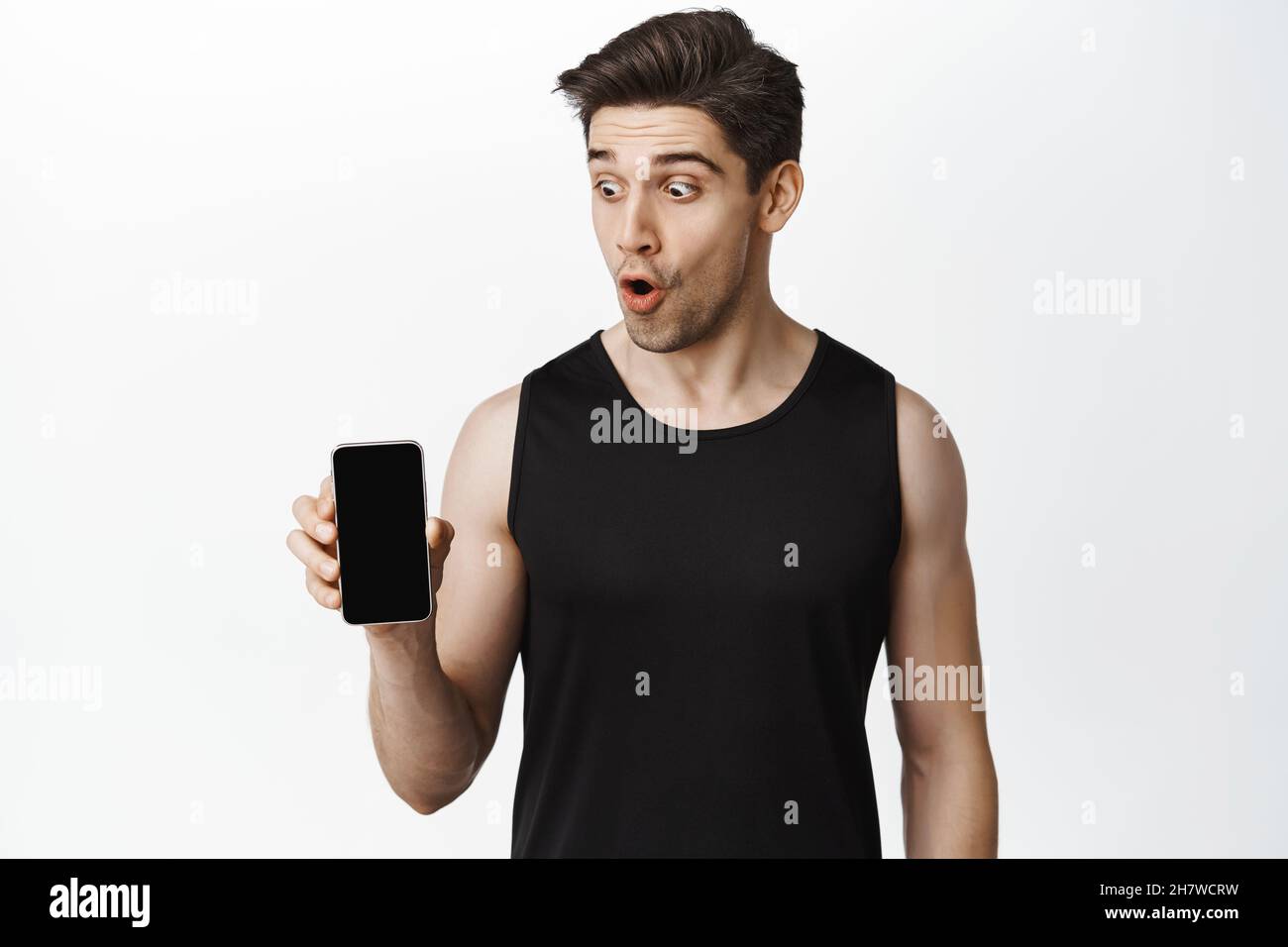 Portrait of athletic guy showing mobile phone screen and looking