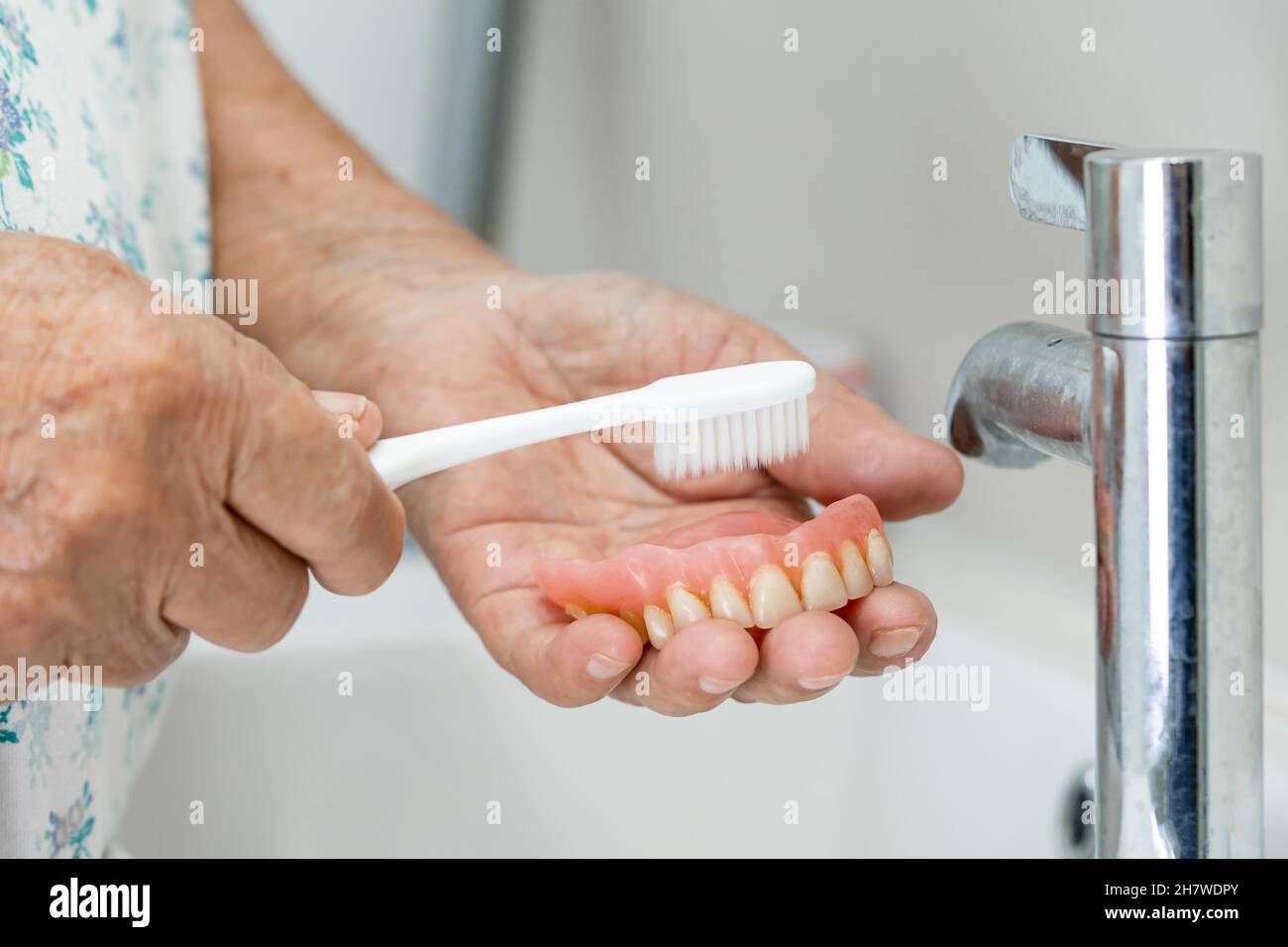 Asian senior or elderly old woman patient use toothbrush to clean partial denture of replacement