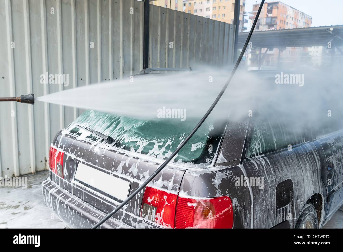 Person washes soap suds from a car with clean water. Car wash Stock