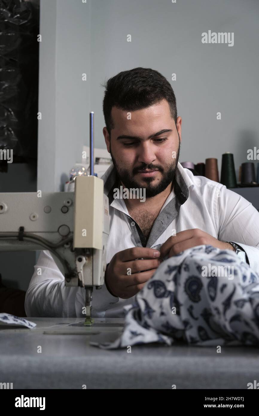 Middle eastern male tailor in white shirt working on sewing machine