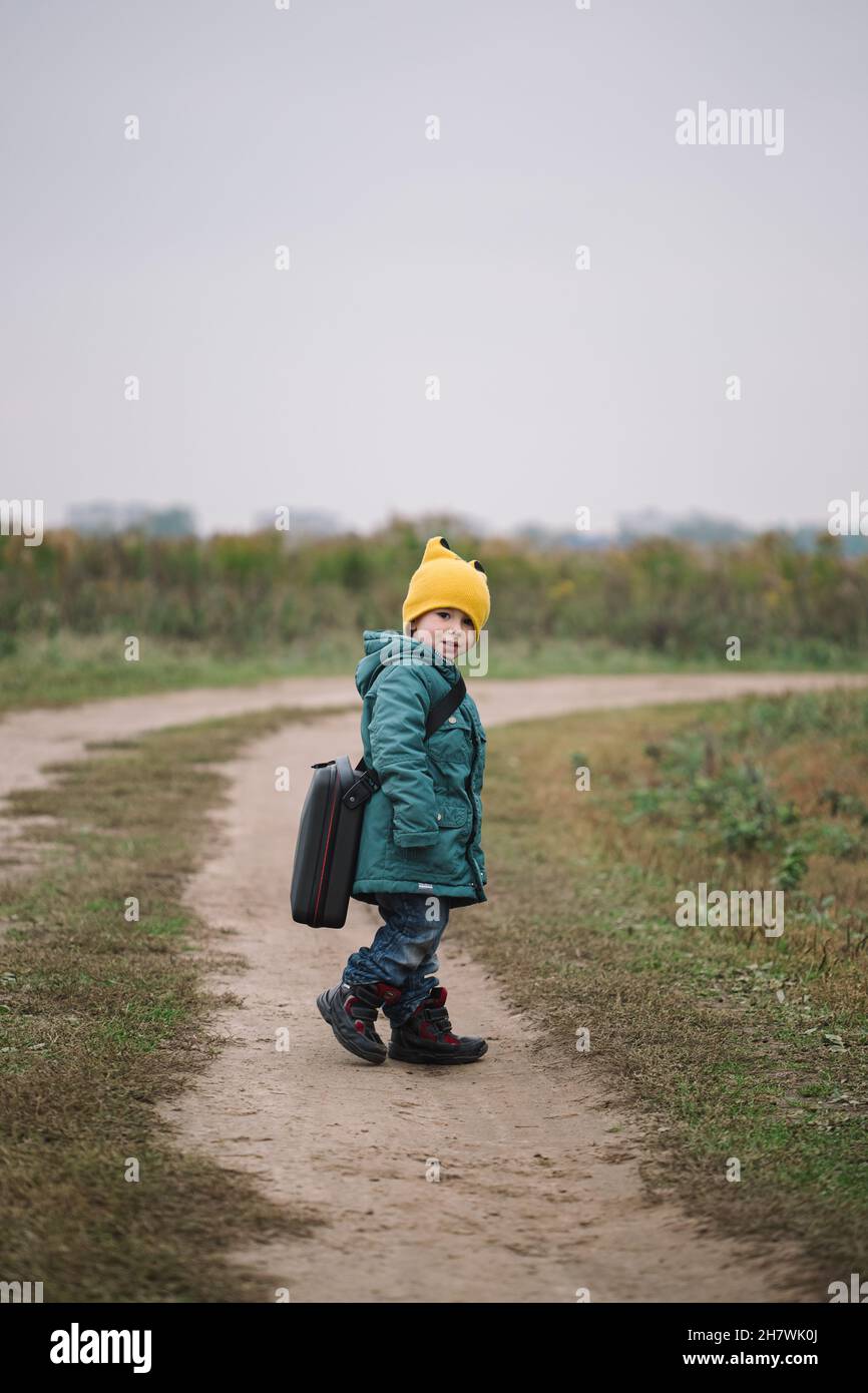 Little caucasian boy carring big case with drone in the field, side view. Stock Photo