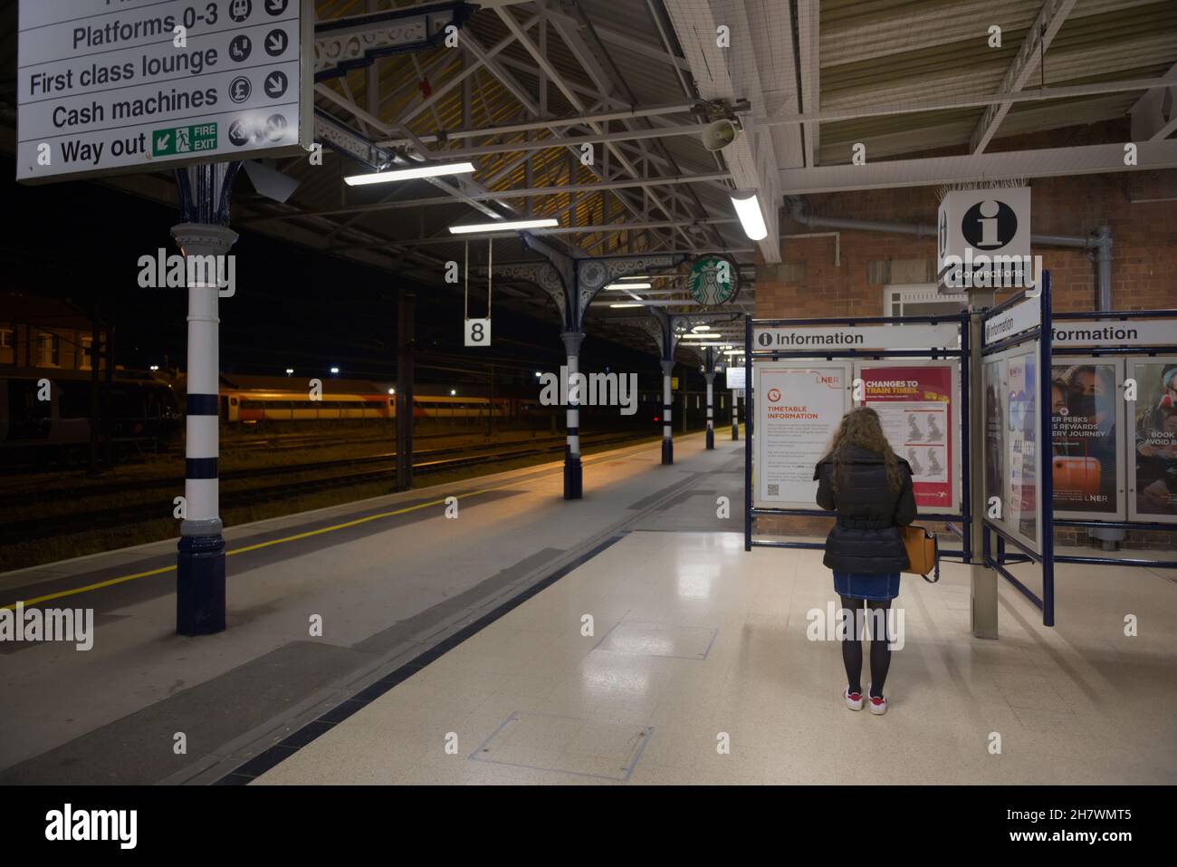 Doncaster, United Kingdom, 22nd May, 2021: Wide angle image of doncaster train station platform number 8 at night. Woman reads information point. Stock Photo