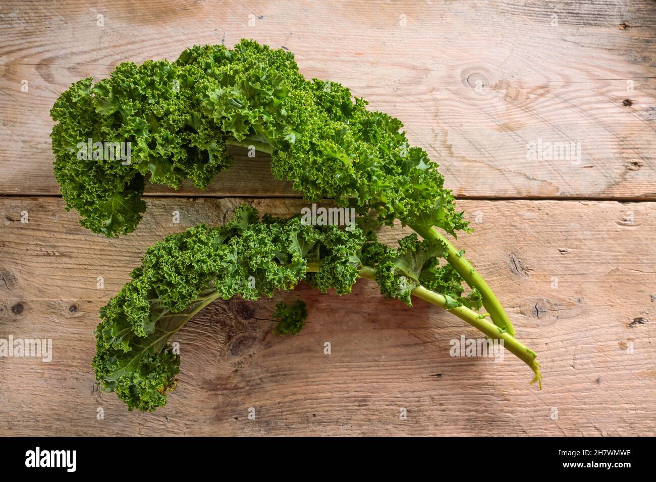 Curly leaves of kale or green leaf cabbage on rustic wooden planks, healthy winter vegetable, copy space, top view from above, selected focus Stock Photo