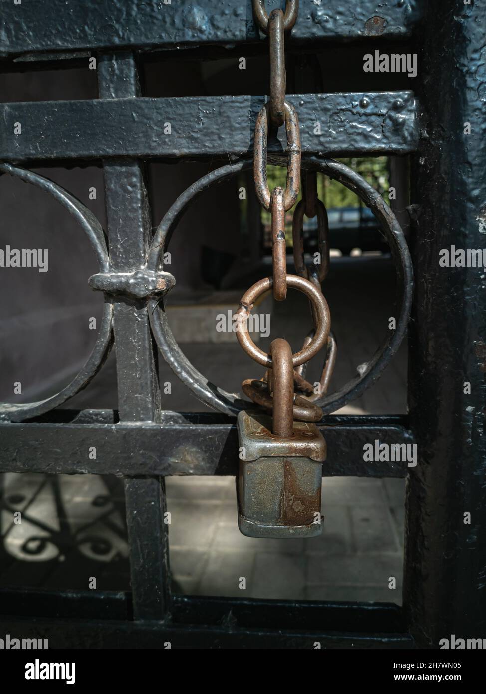 A padlock on a metal chain hanging from an old wrought-iron gate. Elements of the architecture of the old city. Vertical photo. Stock Photo