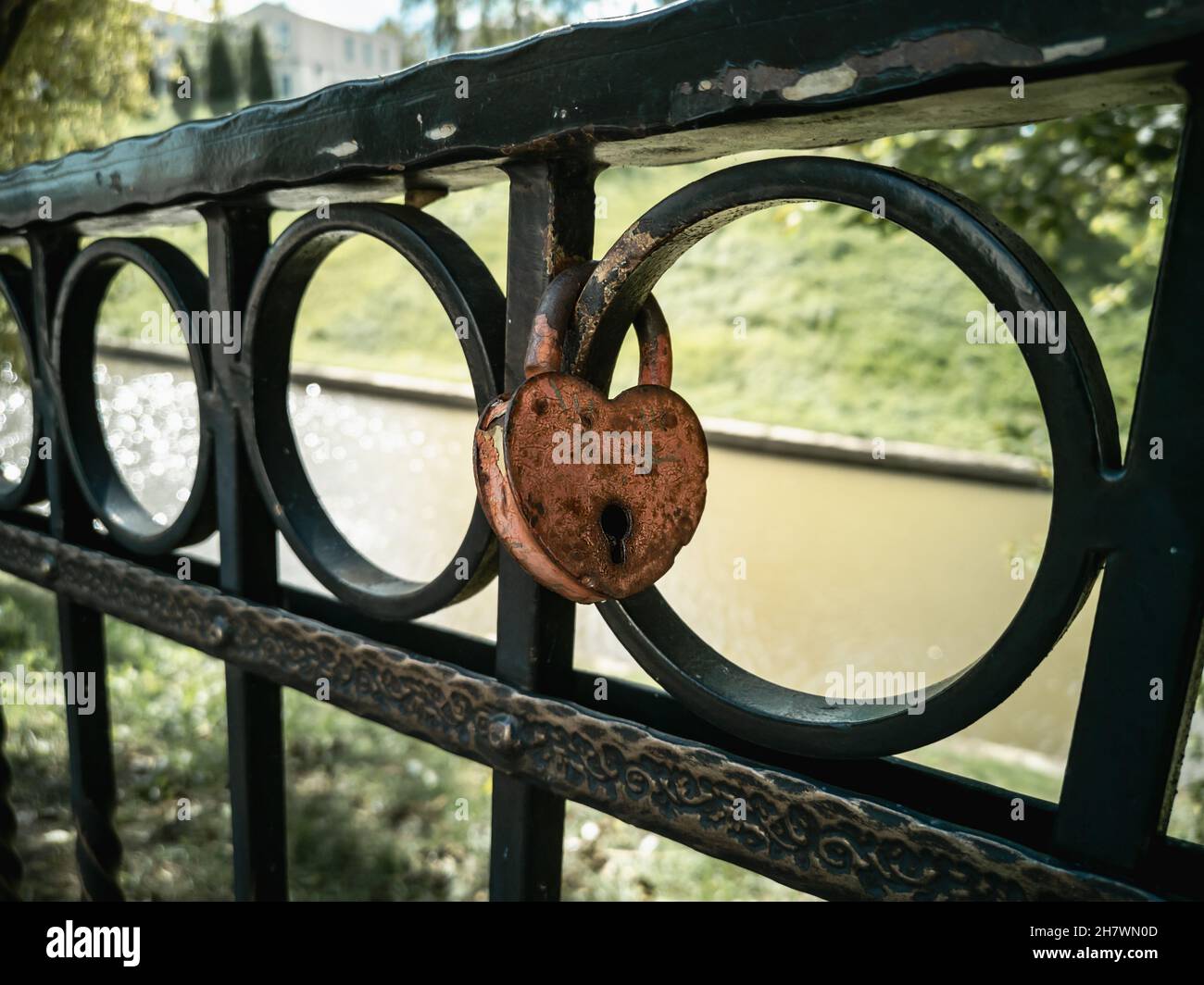 A heart-shaped padlock on a metal antique decorated rail of a bridge ...