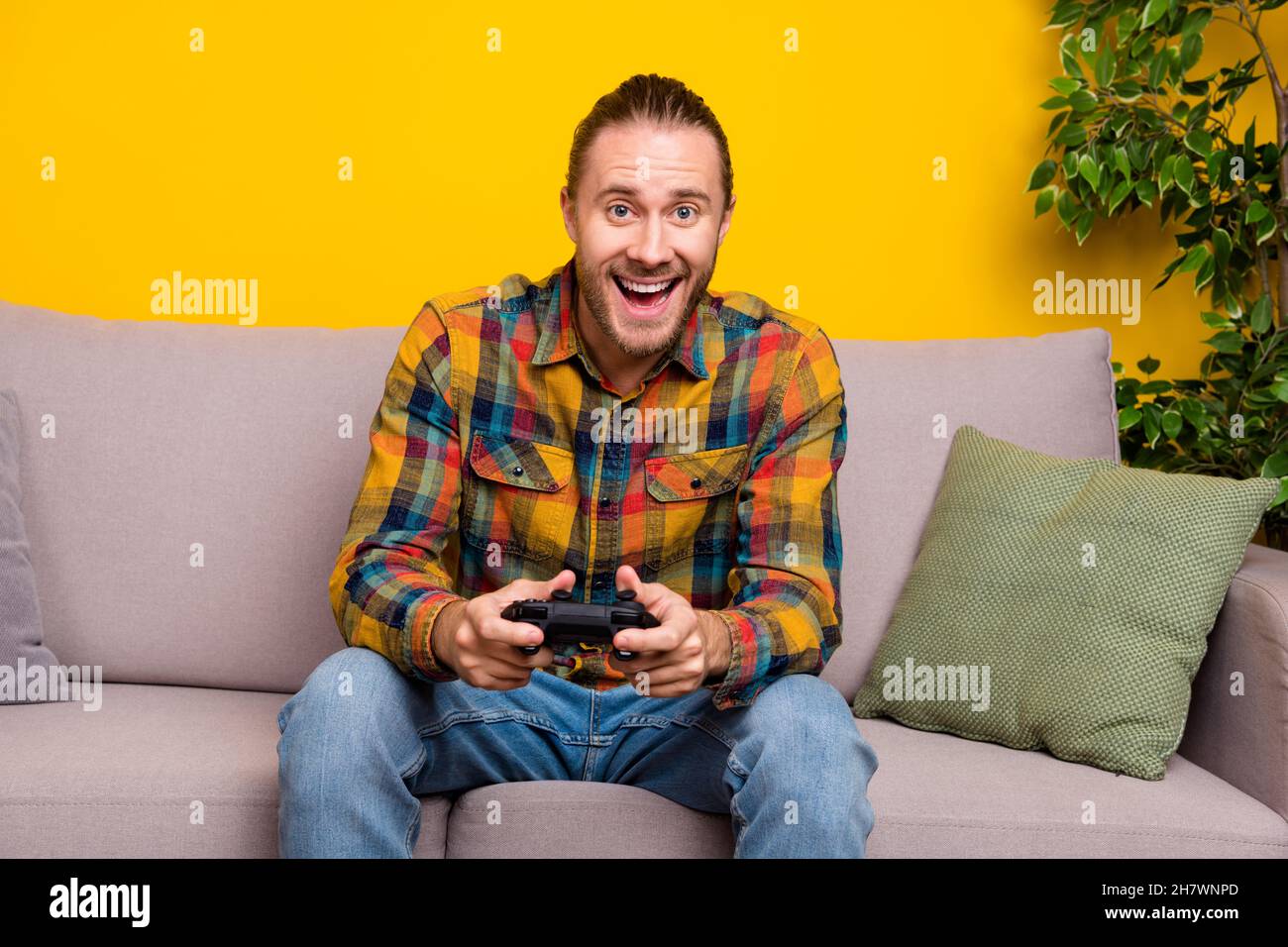 Photo of crazy addicted player guy sit sofa enjoy video game experience wear plaid shirt isolated yellow color background Stock Photo