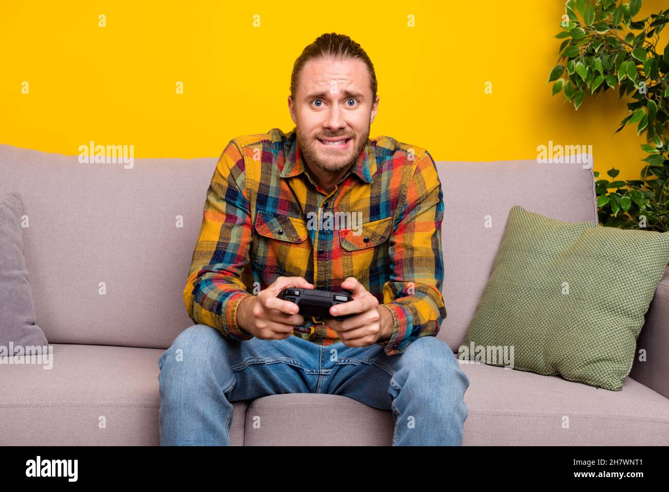 Photo of nervous guy sit divan play intense video game competition wear plaid shirt isolated yellow color background Stock Photo