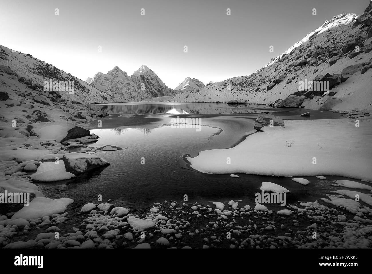 Black and white image of a high mountain lake against a background of snow-covered mountain peaks in the Karachay-Cherkessia Republic Stock Photo