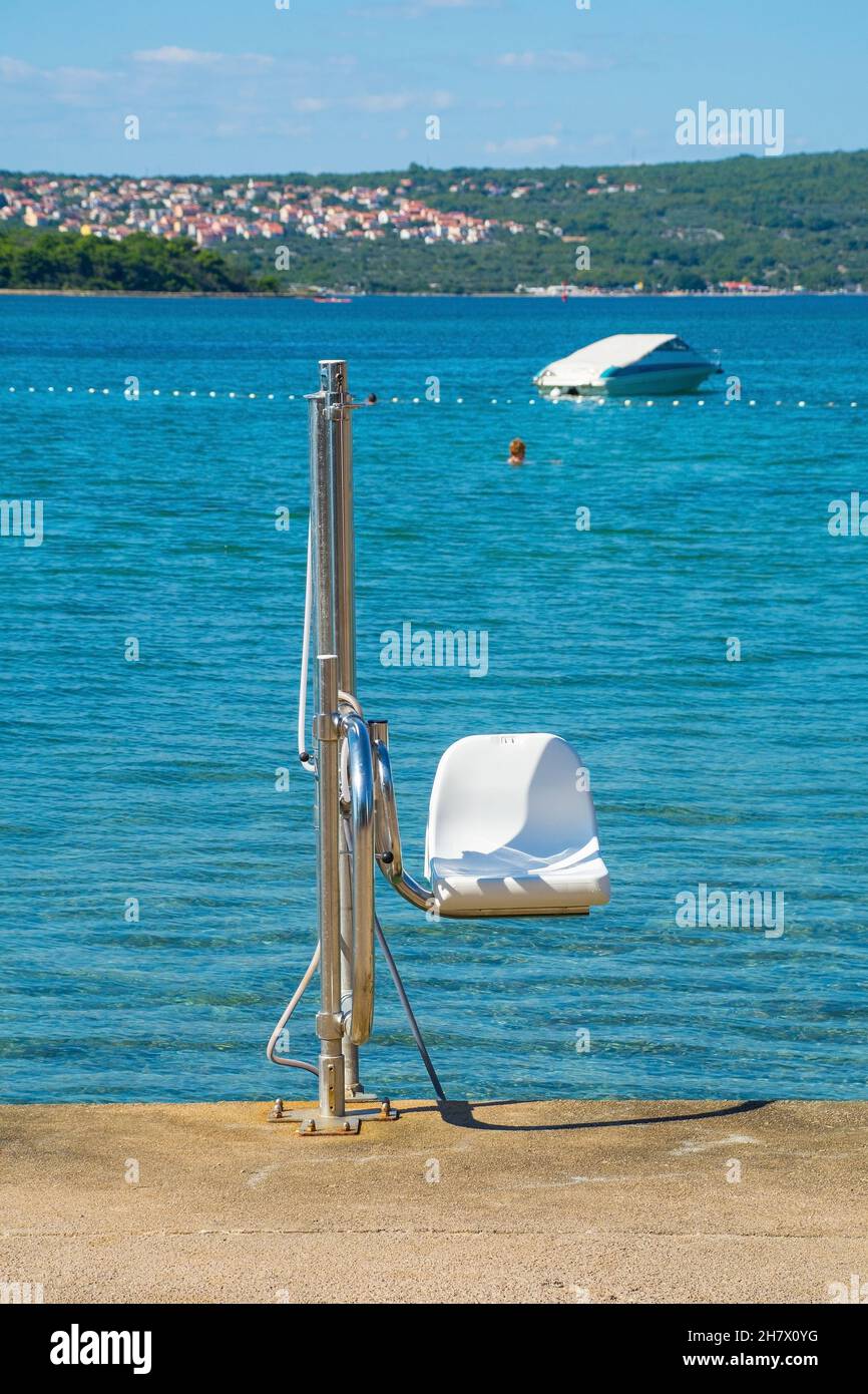 A chair lift for helping disabled people into the sea on the waterfront at Punat on Krk Island in Primorje-Gorski Kotar County in western Croatia Stock Photo