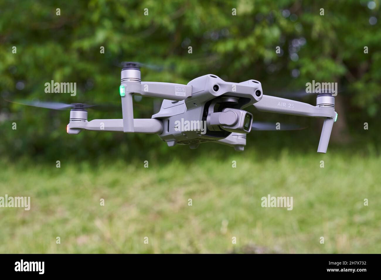 Nürtingen, Germany - June 26, 2021: Gray Dji air 2s drone hovers over the green meadow. Tree in the background. Stock Photo