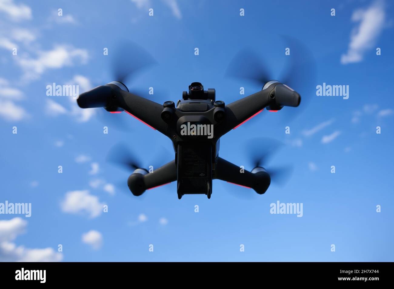 Nürtingen, Germany - June 26, 2021: Black dji fpv drone hovering in front of a blue sky. Racing drone with dark propellers and red lights. Up view. Sy Stock Photo