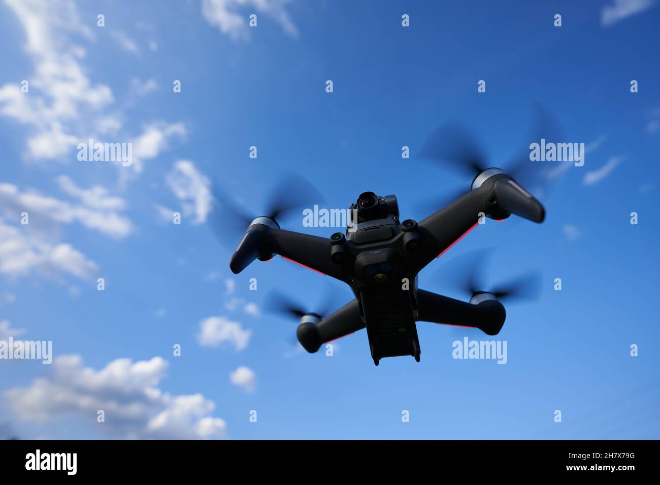Nürtingen, Germany - June 26, 2021: Black dji fpv drone hovering in front of a blue sky. Racing drone with dark propellers and red lights. View Obliqu Stock Photo