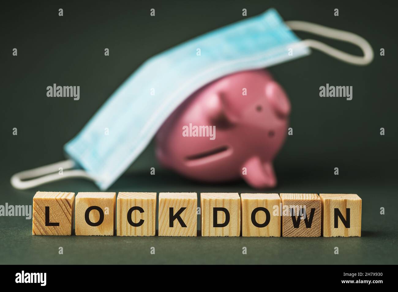 Wooden cubes with text on the background of a medical mask and an inverted piggy bank, a concept on the topic of falling incomes of people during a lo Stock Photo