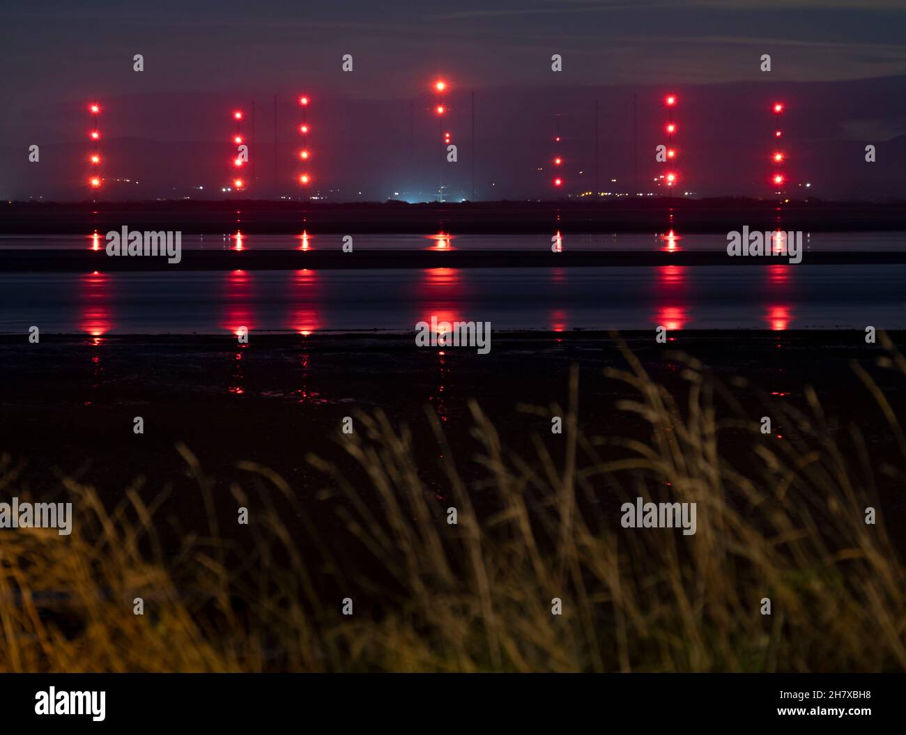 A view of the Anthorn Radio station in Cumbria, ENgland seen from across the Solway Firth, Scotland at night with the lights glowing on the masts. Stock Photo