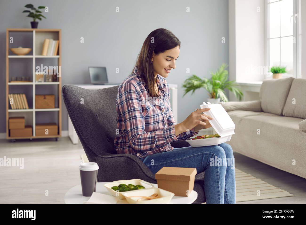 Happy woman opens plastic container with food that was delivered to her