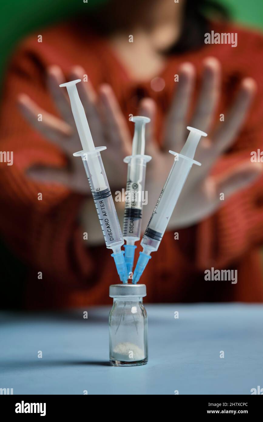 Woman refusing covid-19 vaccine. Anti-vaxxer activist showing stop sign to coronavirus vaccine vial with syringes. Vaccine scepticism. Anti Stock Photo