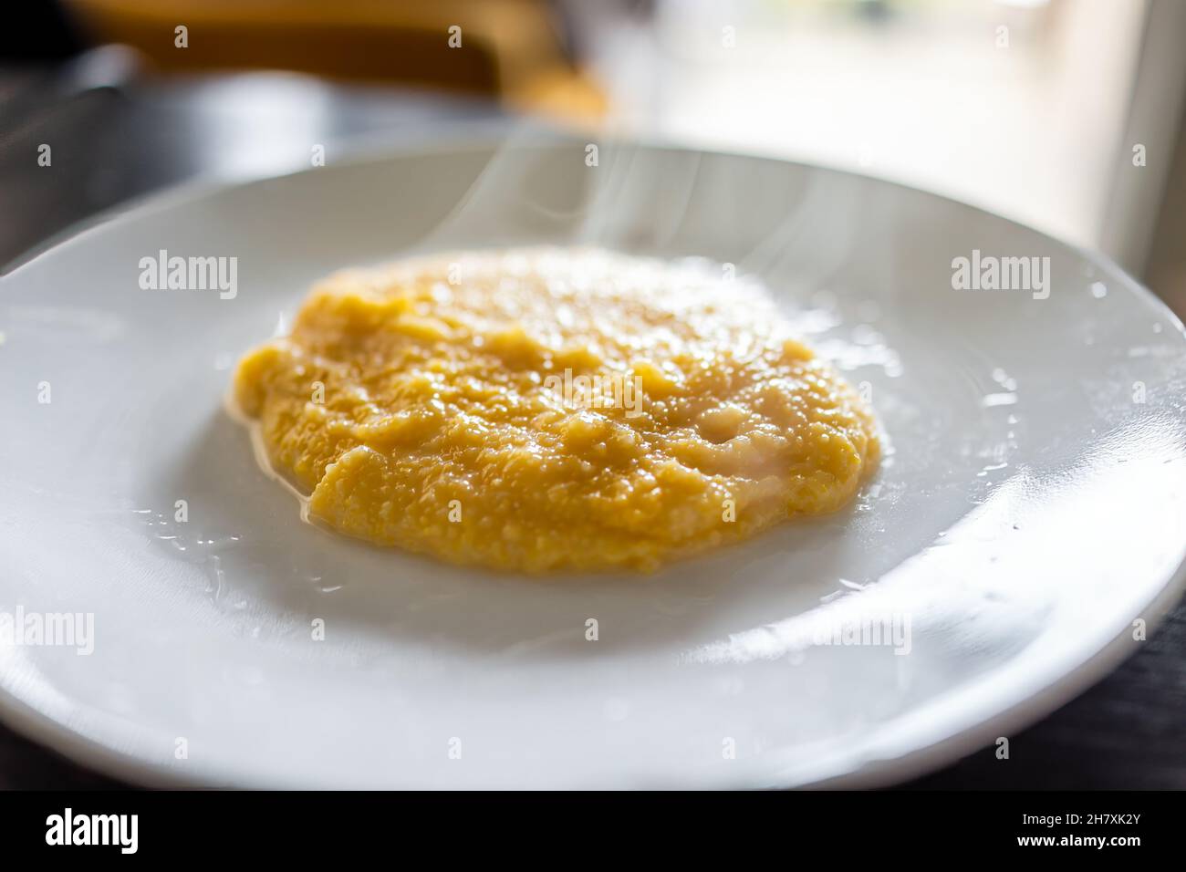 Cooked yellow southern american corn grits on plate as breakfast porridge with hot steam rising and texture of healthy cereal Stock Photo