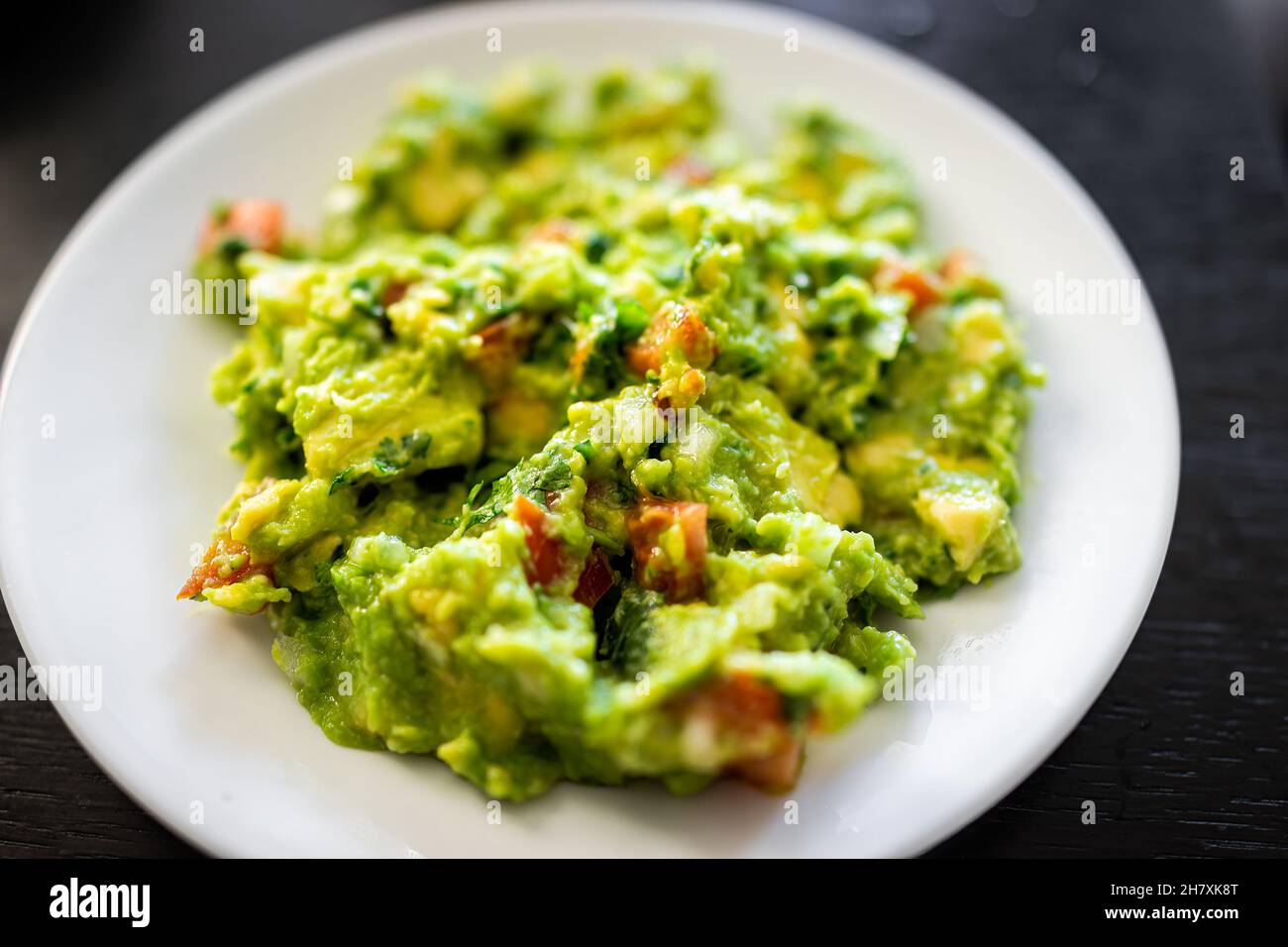 Above macro closeup view of guacamole dish on white plate made with ripe green avocado, garlic tomatoes and cilantro Stock Photo