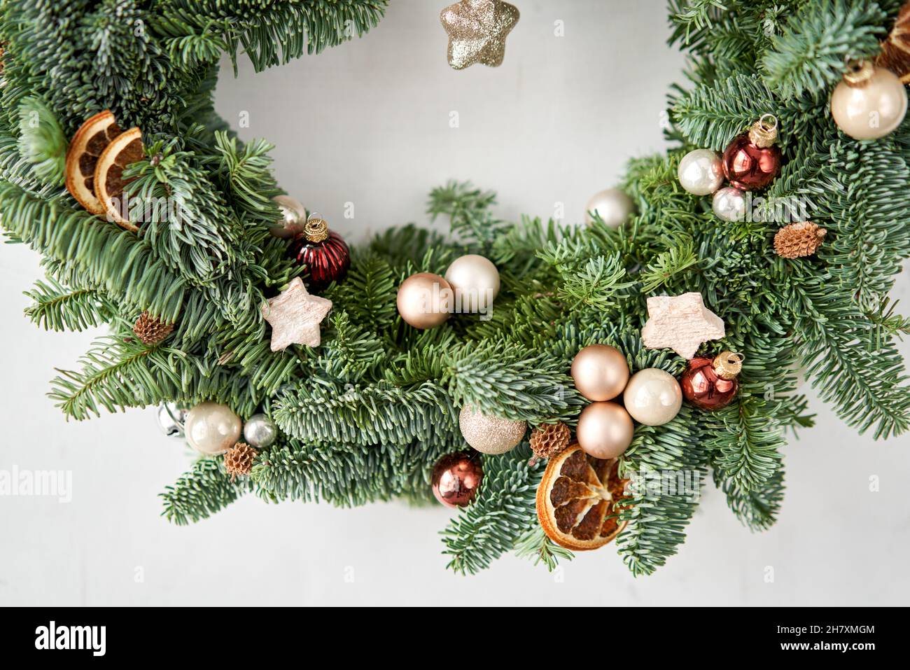 Beautiful festive wreath of fresh spruce on Gray wall. Xmas circlet with red and gold ornaments and balls. Christmas mood. Stock Photo