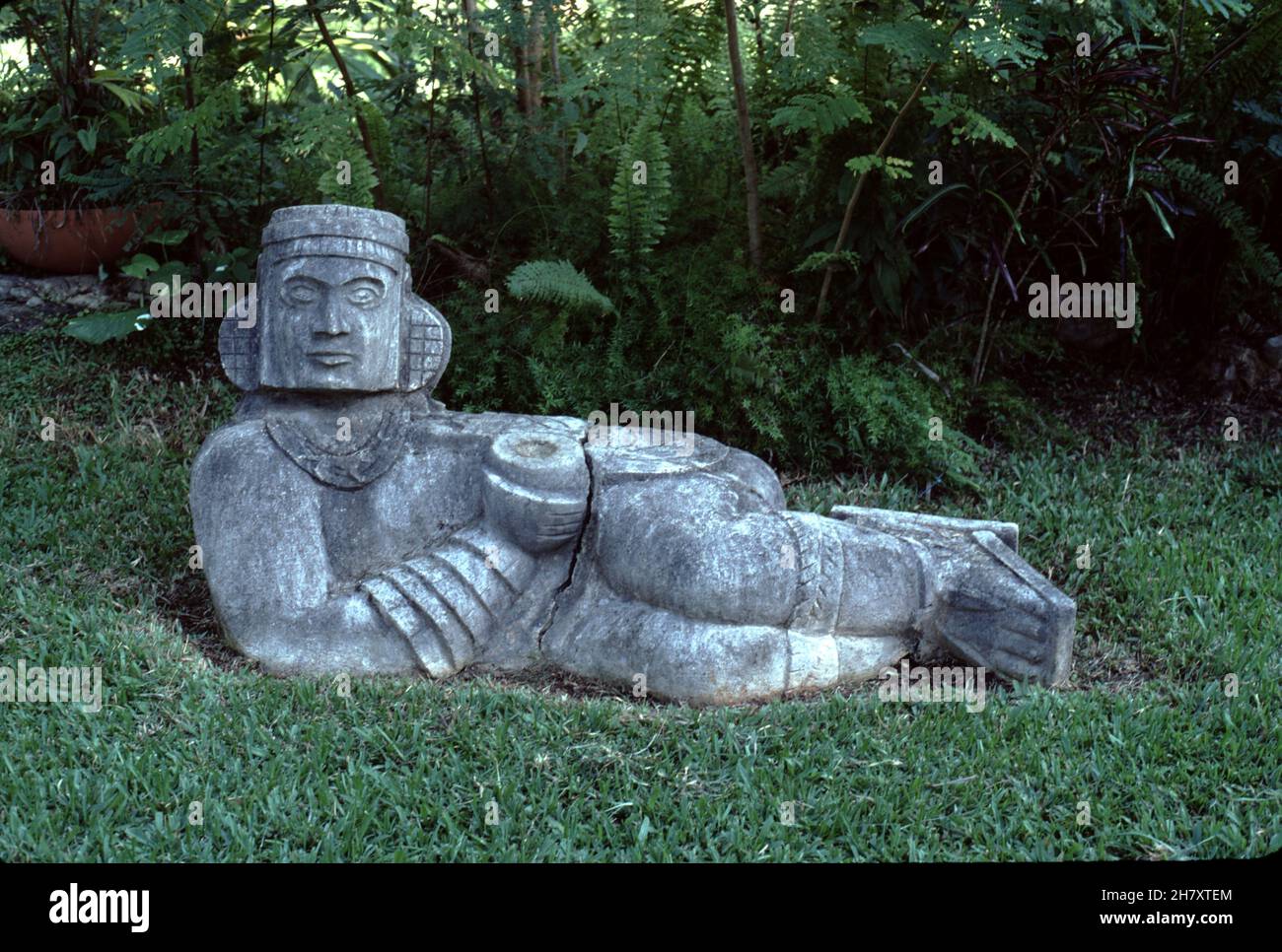 Uxmal Mexico. 12/27/1985. Choc Mool (Chocmool). Pre-Columbian Mesoamerican stone sculpture. A reclining figure with its head facing 90 degrees from the front, supporting itself on its elbows and supporting a bowl or a disk upon its stomach.  Believed to be associated with sacrificial stones or thrones. Stock Photo